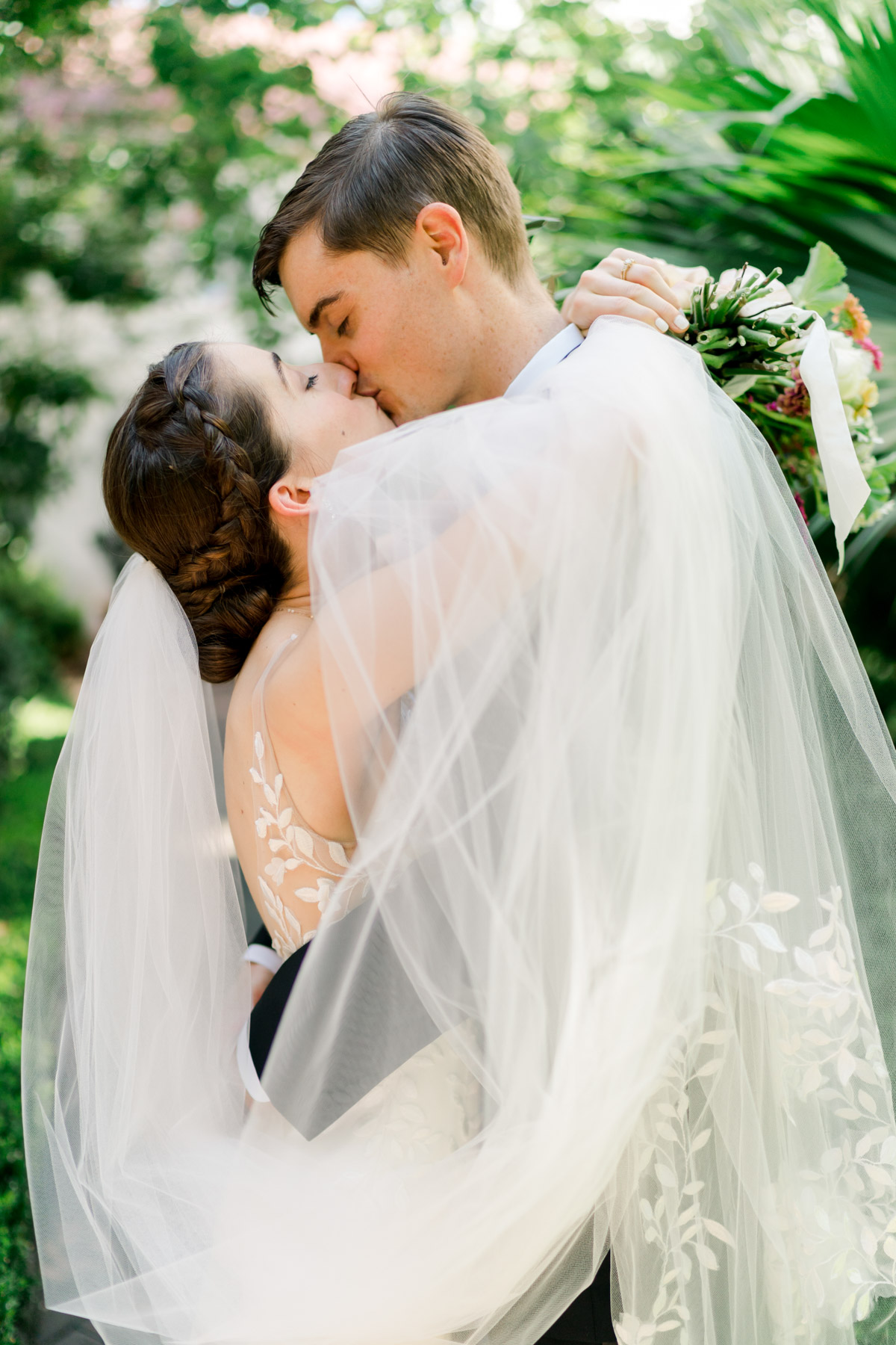 A bride and groom kiss, wrapped in the bride's veil