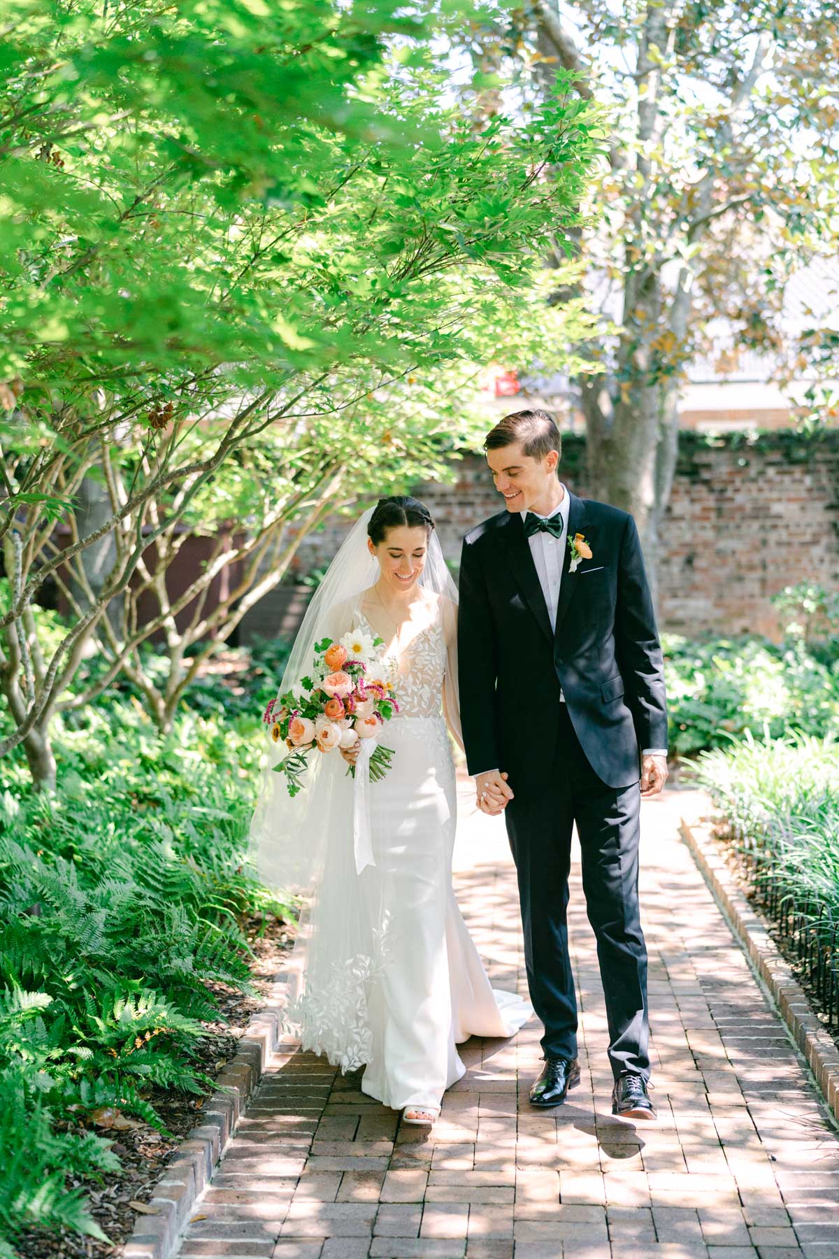 A bride and groom walk together in a courtyard in Charleston, SC
