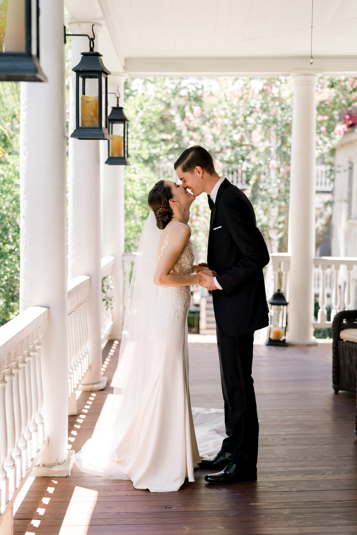 A bride and groom laughing and kissing on a porch at Zero George hotel in Charleston, SC 