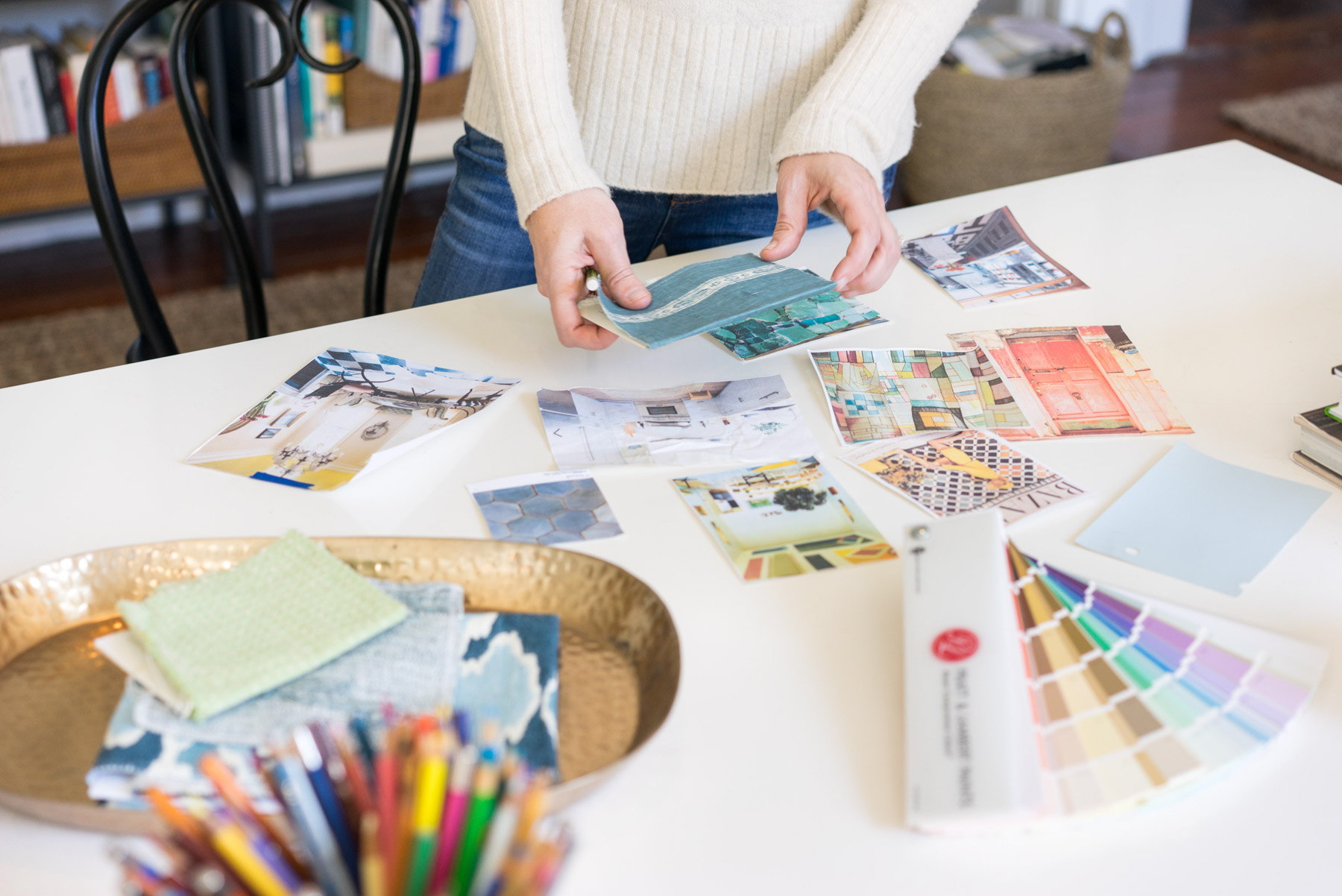 An interior designer sorts through fabric samples, paint colors, and inspiration images on her desk. 