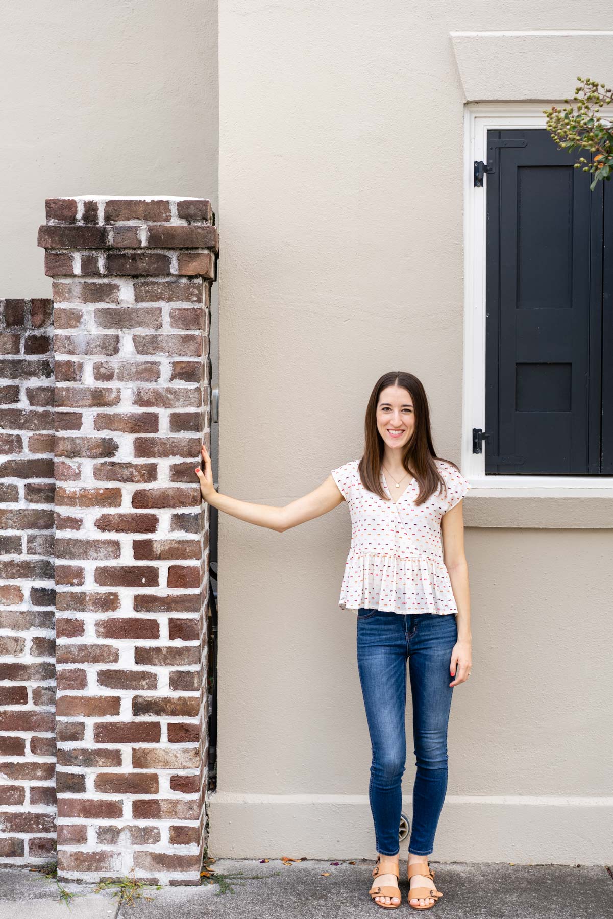 Woman in denim jeans and a white blouse standing near a brick wall demonstrating how not to pose for a photoshoot with her arm outstretched too far