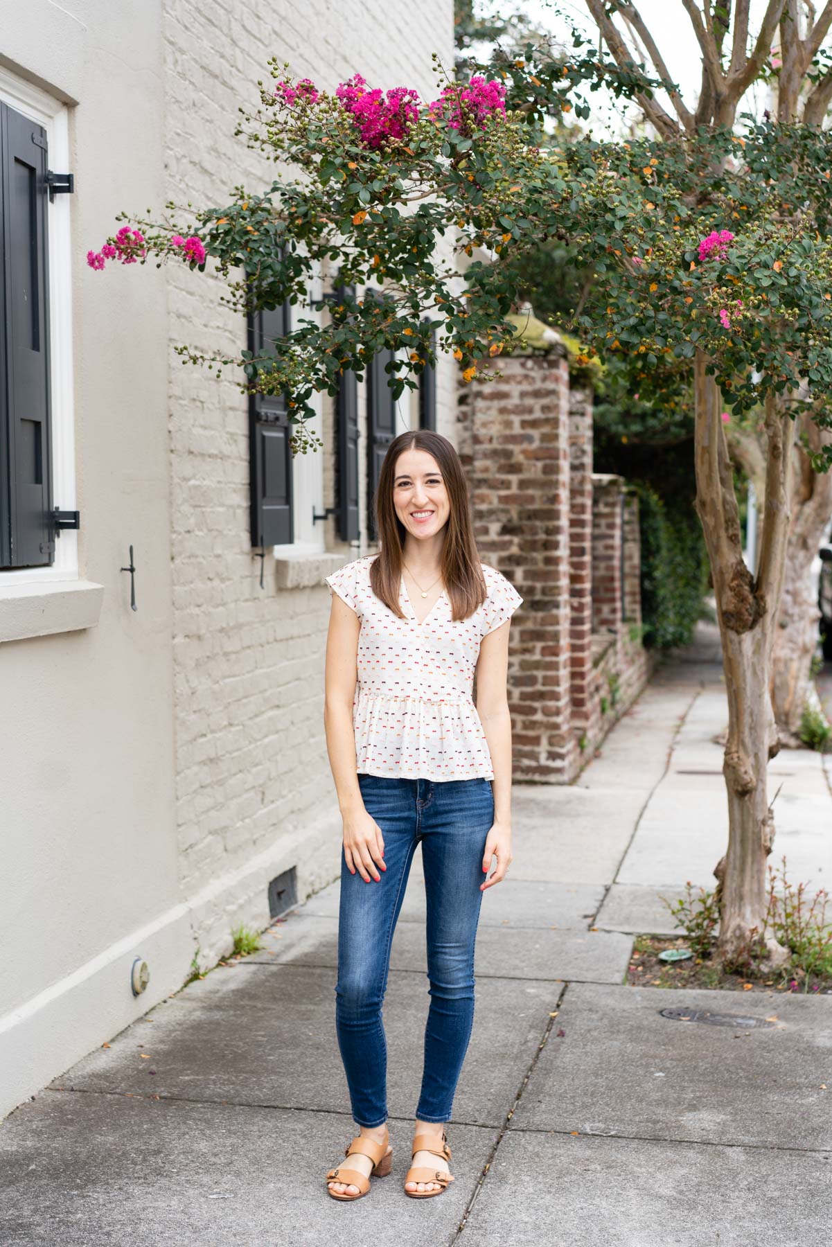 Woman in denim jeans and a white blouse demonstrating how to pose for a photoshoot by shifting her weight to one leg and smiling naturally at the camera