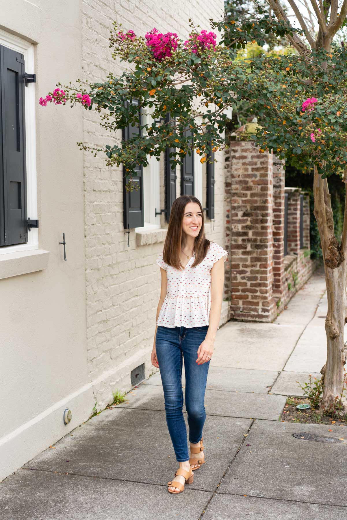 Woman in denim jeans and a white blouse demonstrating how to pose for a photoshoot by walking confidently down the sidewalk smiling and looking natural