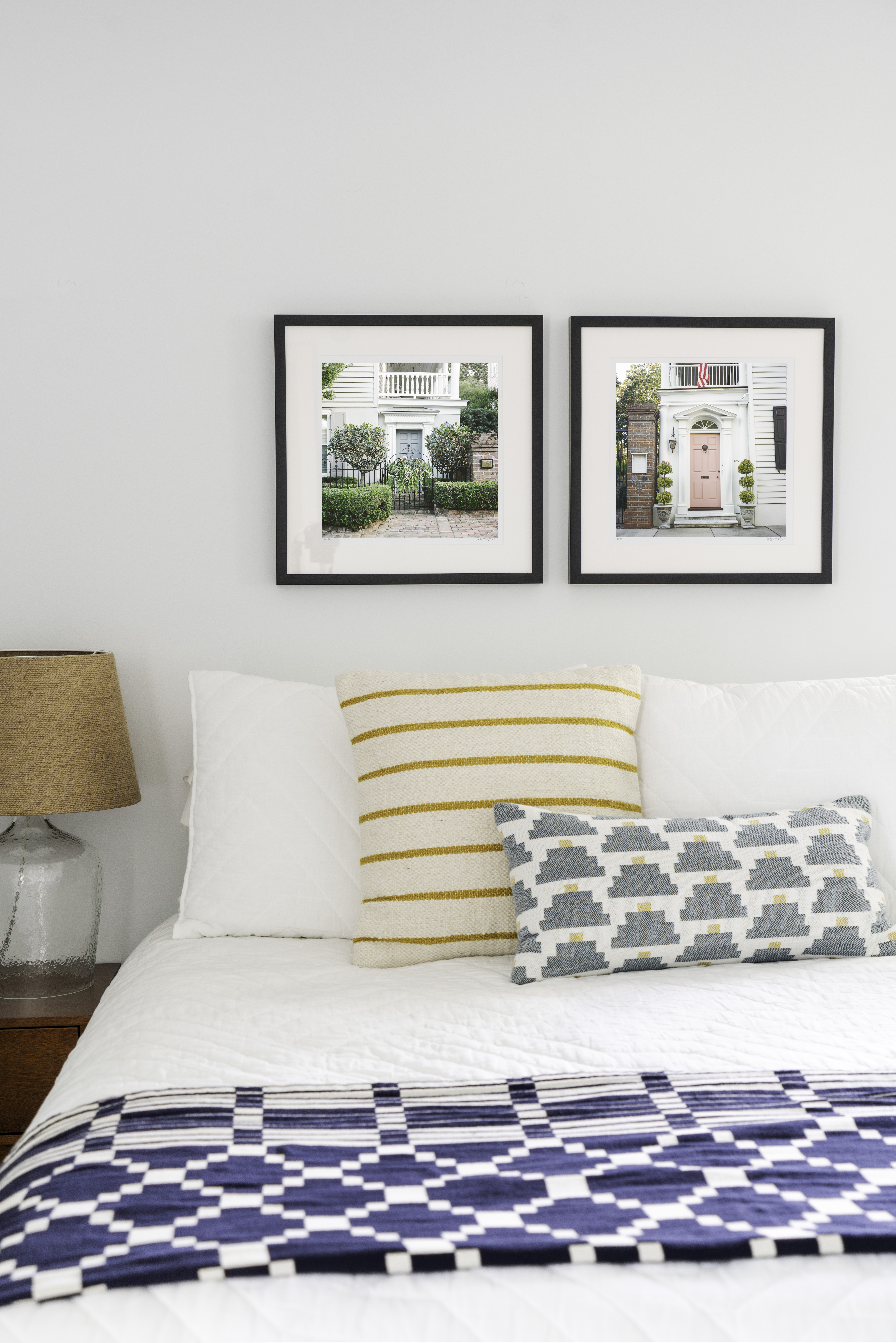 Two photographs of doors in Charleston, South Carolina hanging on the wall above a bed in black frames