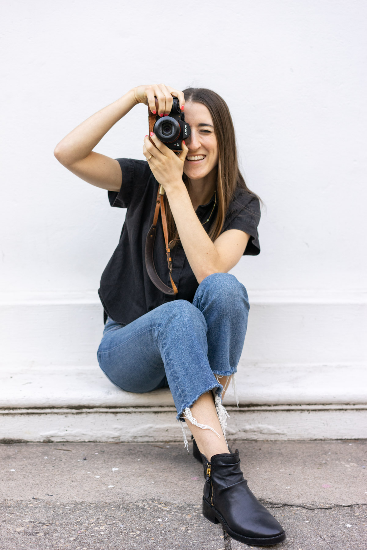 Woman photographer holding a camera up to her eye and smiling as she takes a photo. 
