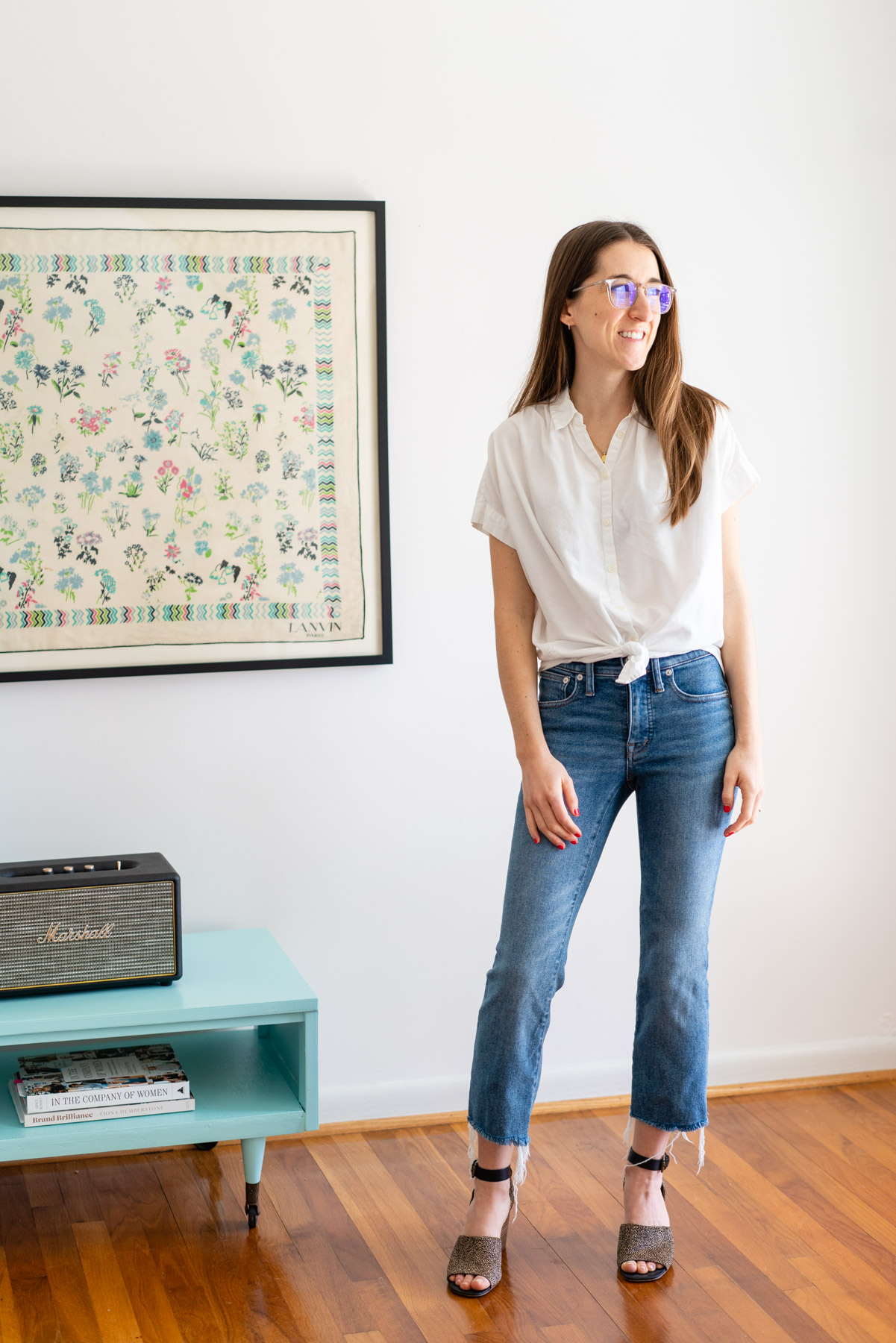 Woman modeling Madewell's Cali Demi Boot jeans with a white button up shirt tied at the waist