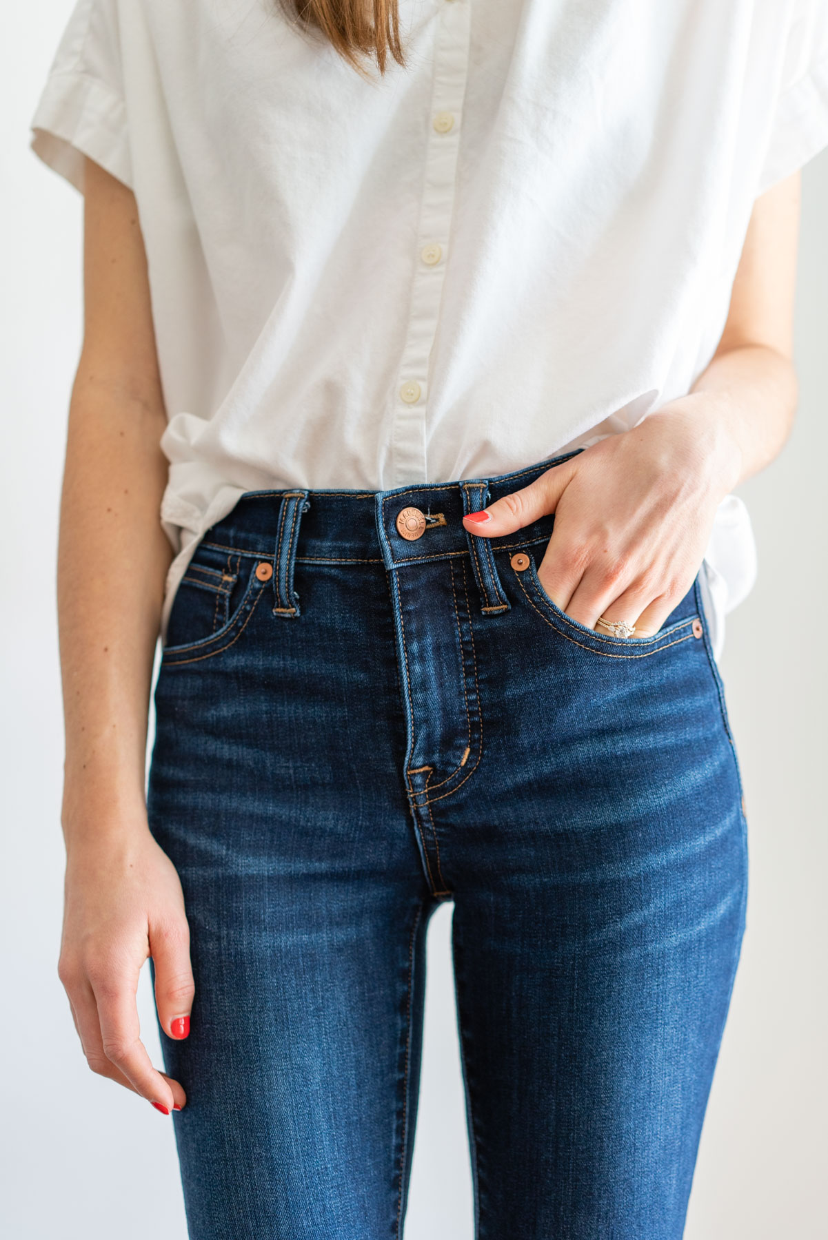 Woman modeling Madewell's dark Skinny jeans for a Madewell jeans review with a white button up shirt tied at the waist
