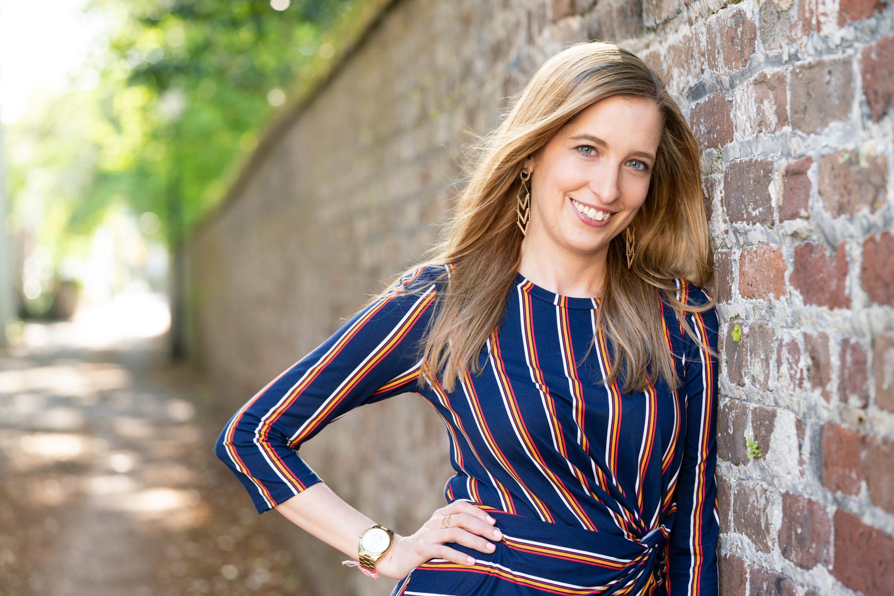 Headshot of a woman in a striped dress leaning against a brick wall in downtown Charleston, South Carolina