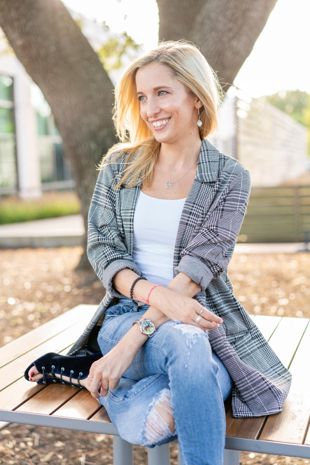Woman in plaid blazer and ripped jeans sitting on top of a picnic table 