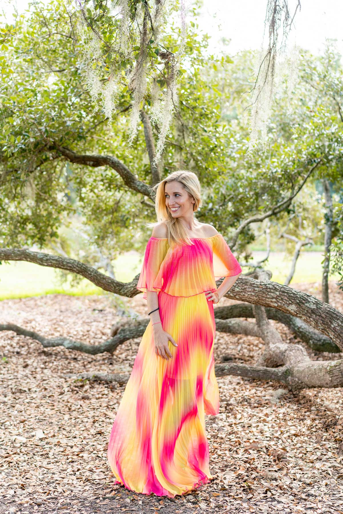 Woman in a pink and yellow floor-length dress posing by an oak tree in Charleston, South Carolina's Hampton Park