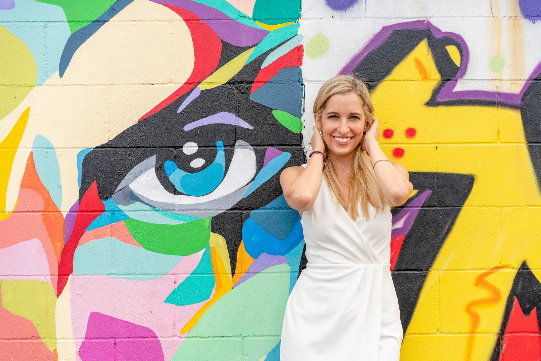 Woman in a white dress posing in front of a graffiti mural wall