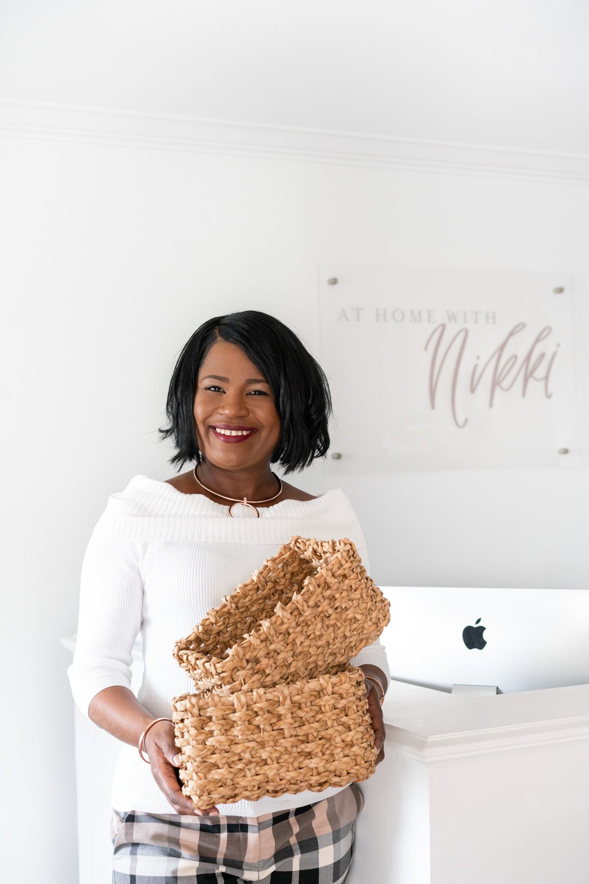 A portrait of professional organizer At Home with Nikki holding two natural woven baskets in front the branded sign in her office. This portrait is an example of how to use props in a personal brand photoshoot. 