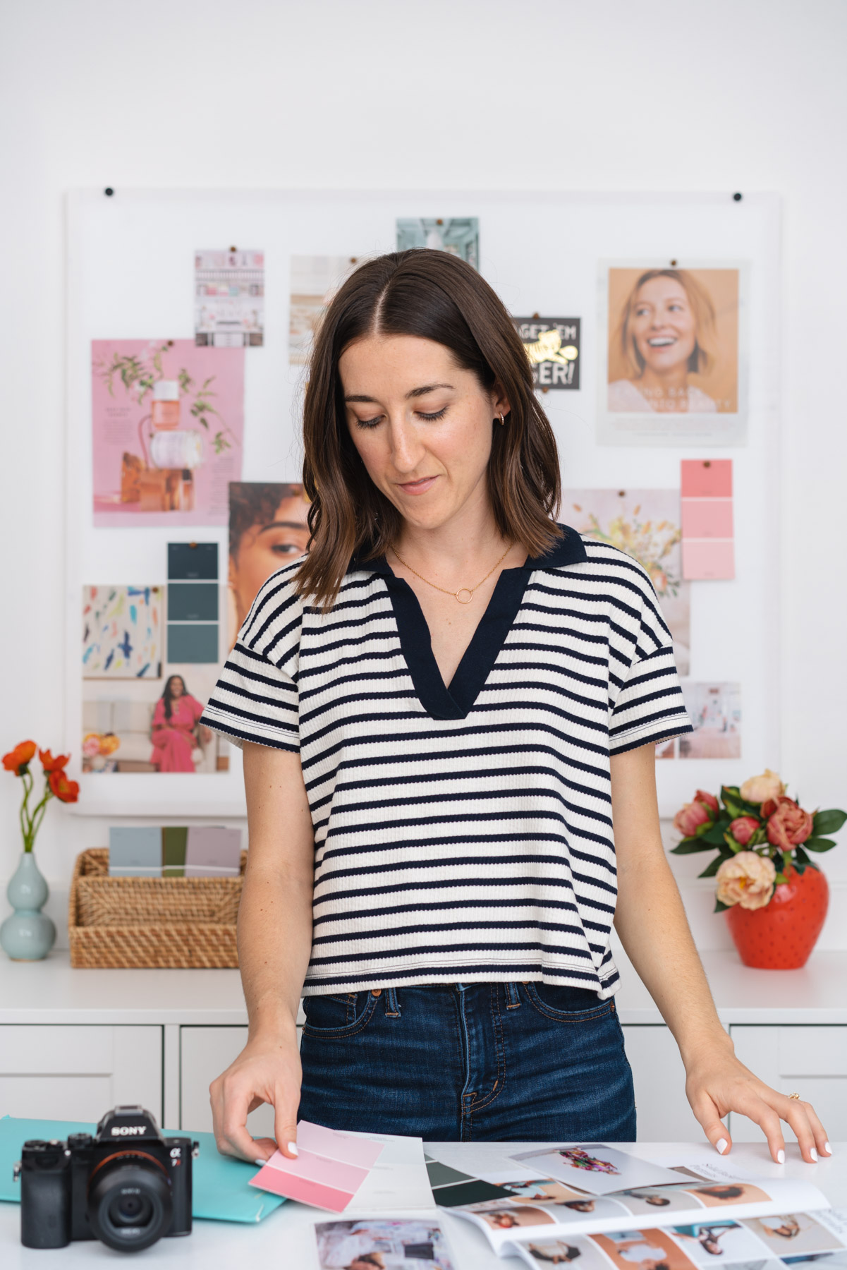 Brand photo of photographer Abby Murphy standing at her desk in front of a mood board. She is looking through brand photoshoot inspiration and color palettes. 