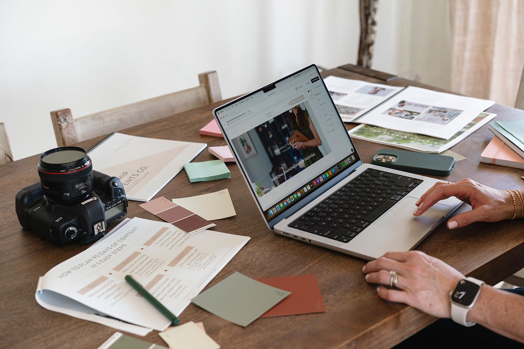 Image of a desk with papers, notebooks, and a laptop with hands on it typing. 